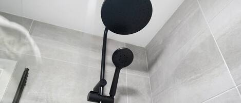 A shower with a roundhead showerhead mounted on a wall, a handheld showerhead attached to a flexible hose, and a vertical bar for support.
