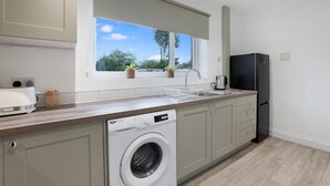 Eine moderne Küche mit integriertem Waschmaschine, Spüle und Fenster mit Blick auf Bäume.