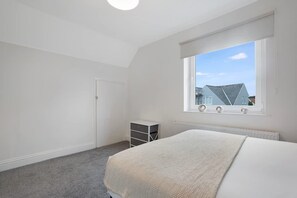 A bedroom with a large window, a bed, a radiator, and a small storage unit. - 3BR in County Durham With Wifi and Street Parking (Durham)