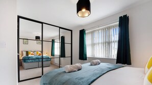 A modern bedroom with a large bed, a mirror, a window with curtains, and a hanging light fixture. - Modern Stockton Retreat Sleeps 6 by Stay With Us (Stockton-on-Tees)