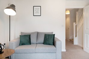 A neutral-colored sofa with two pillows, a floor lamp, and a framed quote on the wall. - Modern Stockton Retreat Sleeps 6 by Stay With Us (Stockton-on-Tees)