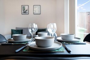 A dining table set with bowls, glasses, and cutlery, with a view of the outdoors through a window. - Modern Stockton Retreat Sleeps 6 by Stay With Us (Stockton-on-Tees)