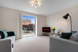A living room with a television displaying 'NETFLIX', a sofa, a coffee table, and a lamp. - Modern Stockton Retreat Sleeps 6 by Stay With Us (Stockton-on-Tees)