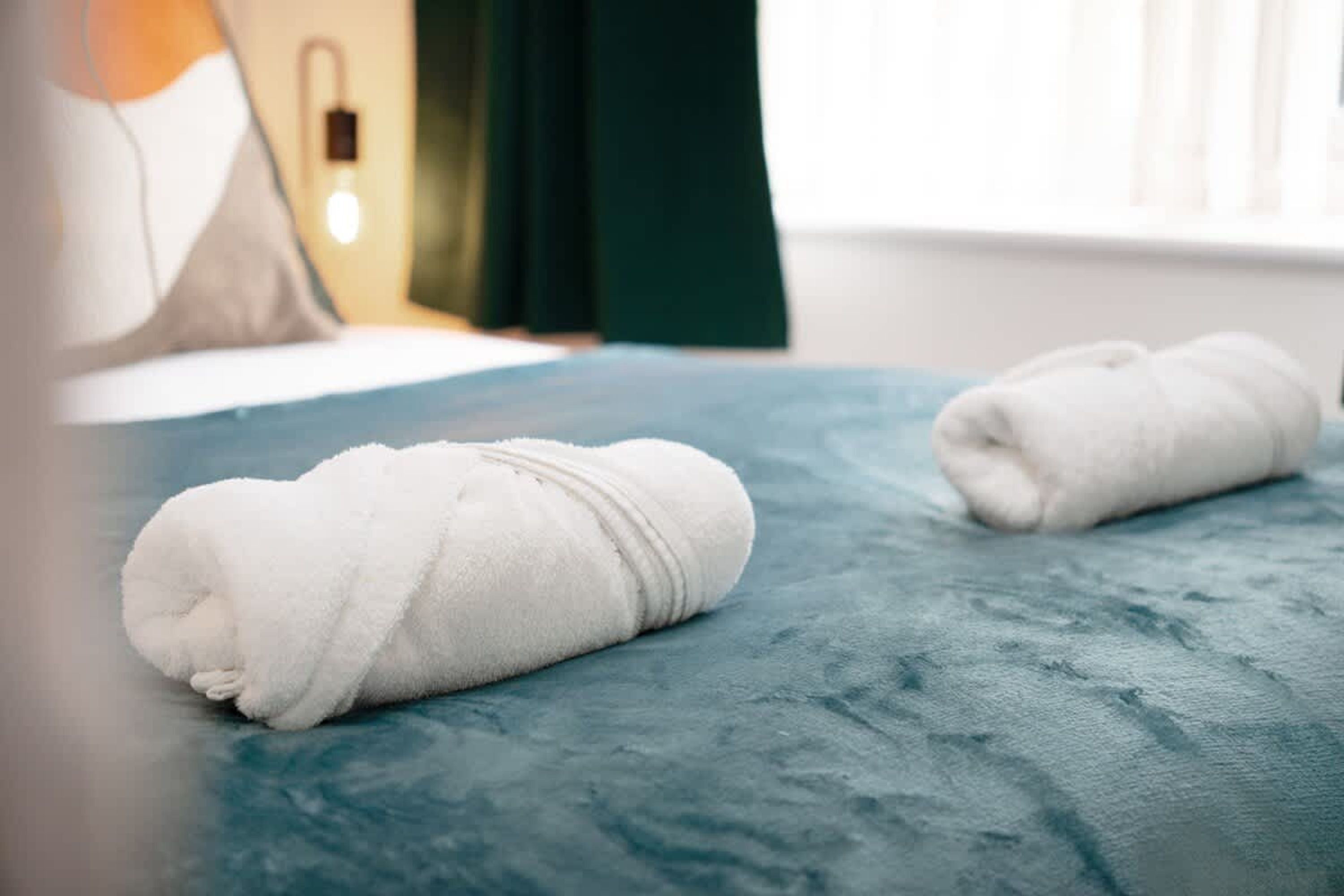 A bed with two neatly rolled white towels and a wall-mounted light fixture.
