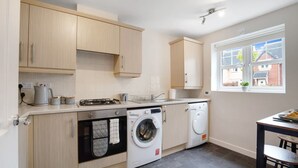 A compact kitchen with a washing machine, a sink, and a window with a view of houses. - Modern Stockton Retreat Sleeps 6 by Stay With Us (Stockton-on-Tees)