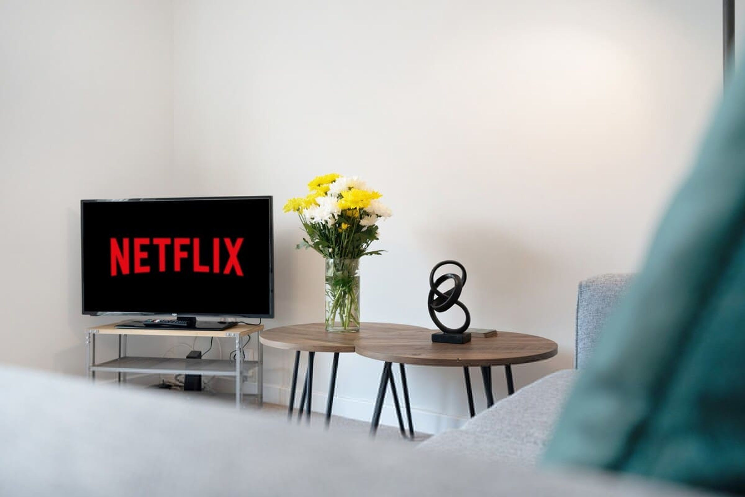 Olohuoneessa on televisio, jonka näytöllä näkyy Netflixin logo, maljakko kukkineen ja moderni veistos pienellä pöydällä.