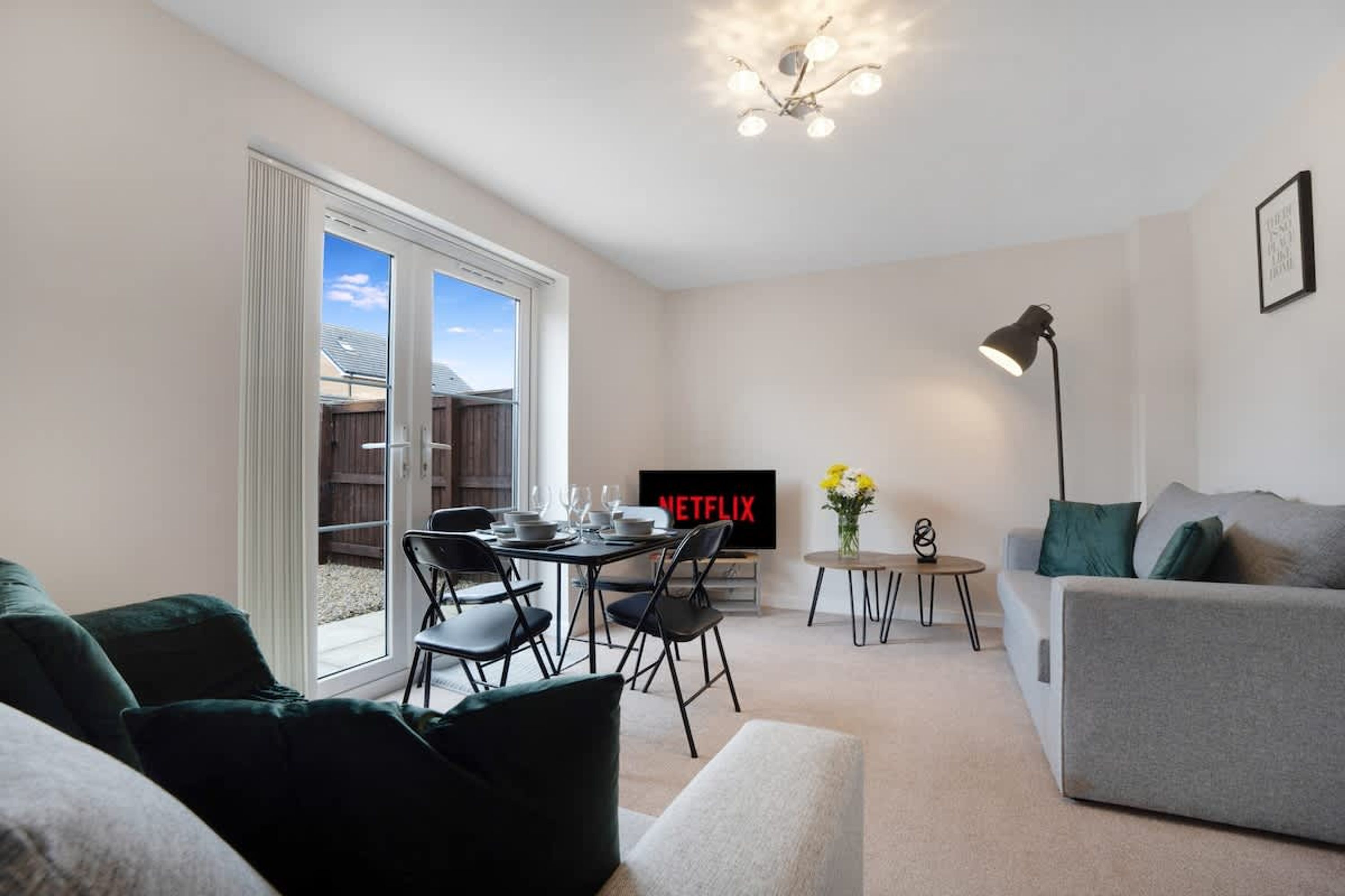 A modern living room with a dining area, a flat-screen TV, and a ceiling light fixture.