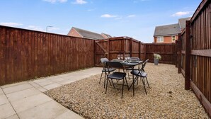 A backyard with a gravel patio, a wooden fence, and a table set for dining. - Modern Stockton Retreat Sleeps 6 by Stay With Us (Stockton-on-Tees)