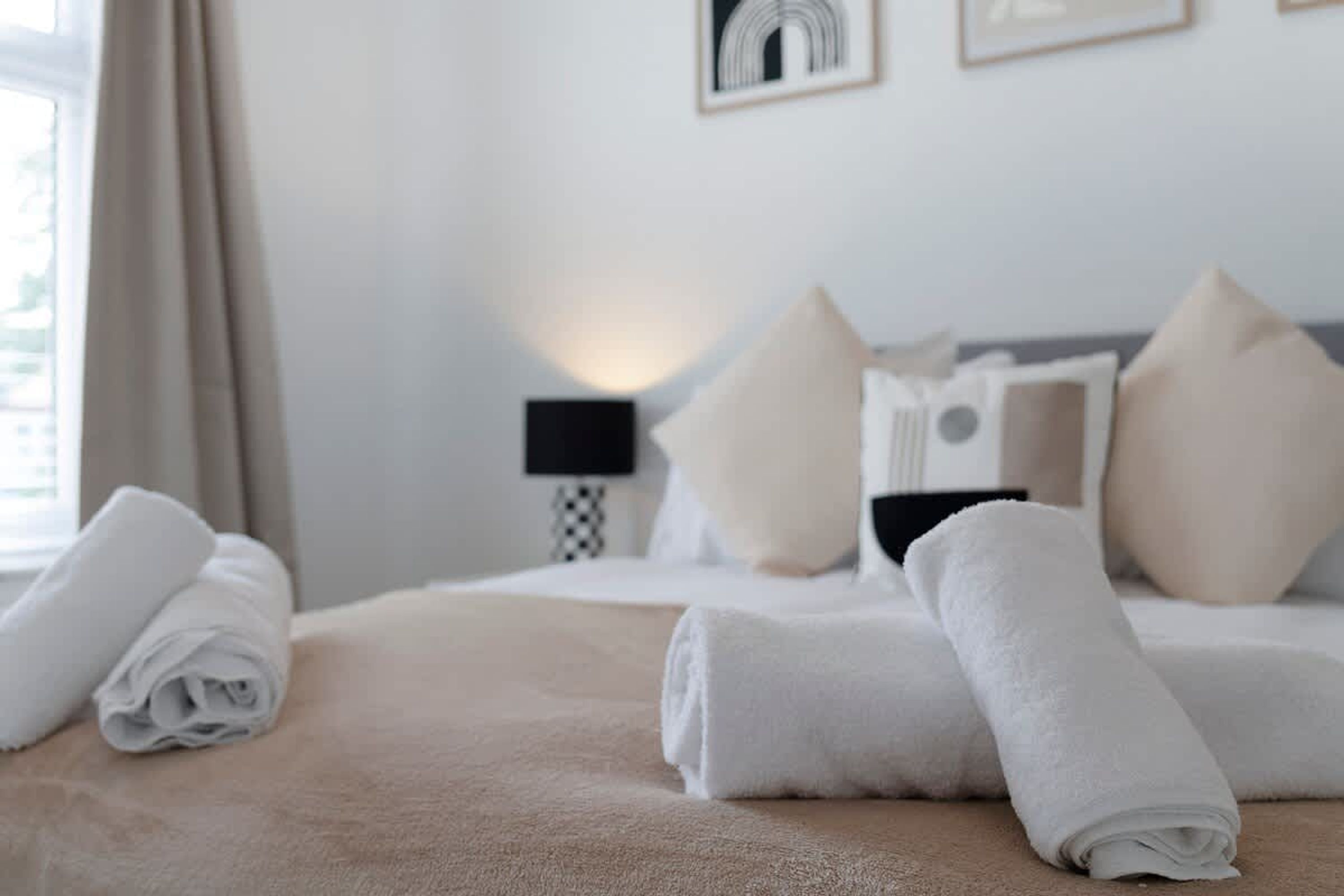A neatly made bed with rolled towels, a bedside lamp, and a wall with framed artwork.