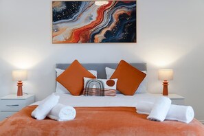 A hotel room with a bed, two nightstands, a painting, and a view of the city. - 2BR Darlington Home by Stay With Us (Darlington)