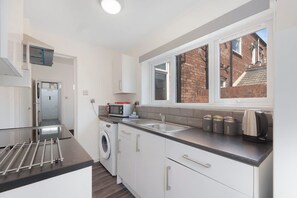 A compact kitchen with a washing machine, a microwave, and a kettle. - 2BR Darlington Home by Stay With Us (Darlington)
