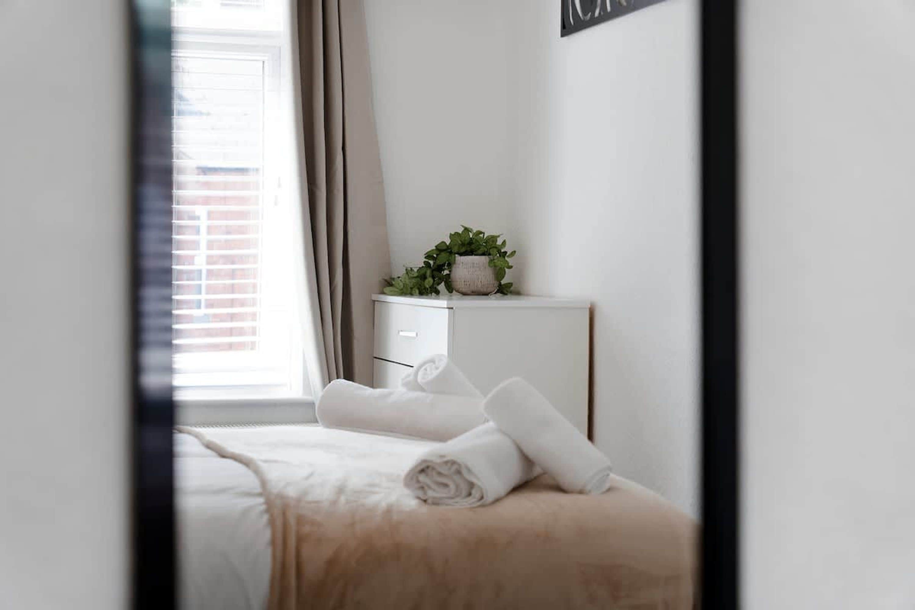 Une chambre d’hôtel avec un lit, une table de chevet ornée d’une plante et une fenêtre avec des rideaux.