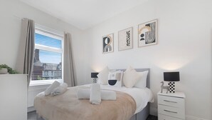 A modern bedroom with a bed, bedside tables, and artwork on the wall. - 2BR Darlington Home by Stay With Us (Darlington)