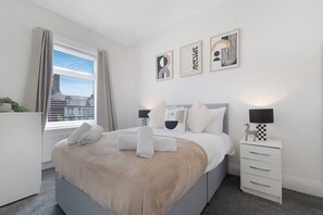 A modern bedroom with a bed, bedside tables, and artwork on the wall. - 2BR Darlington Home by Stay With Us (Darlington)