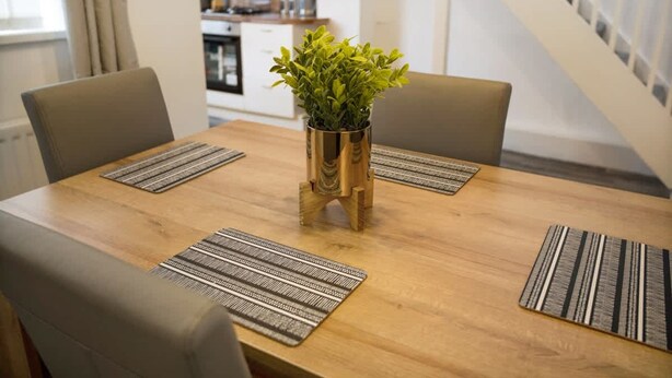 Una mesa de comedor con cuatro sillas, una planta en el centro y manteles individuales estampados.