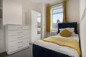 Une chambre à coucher avec un lit, une armoire, une table de chevet et une fenêtre avec des rideaux.