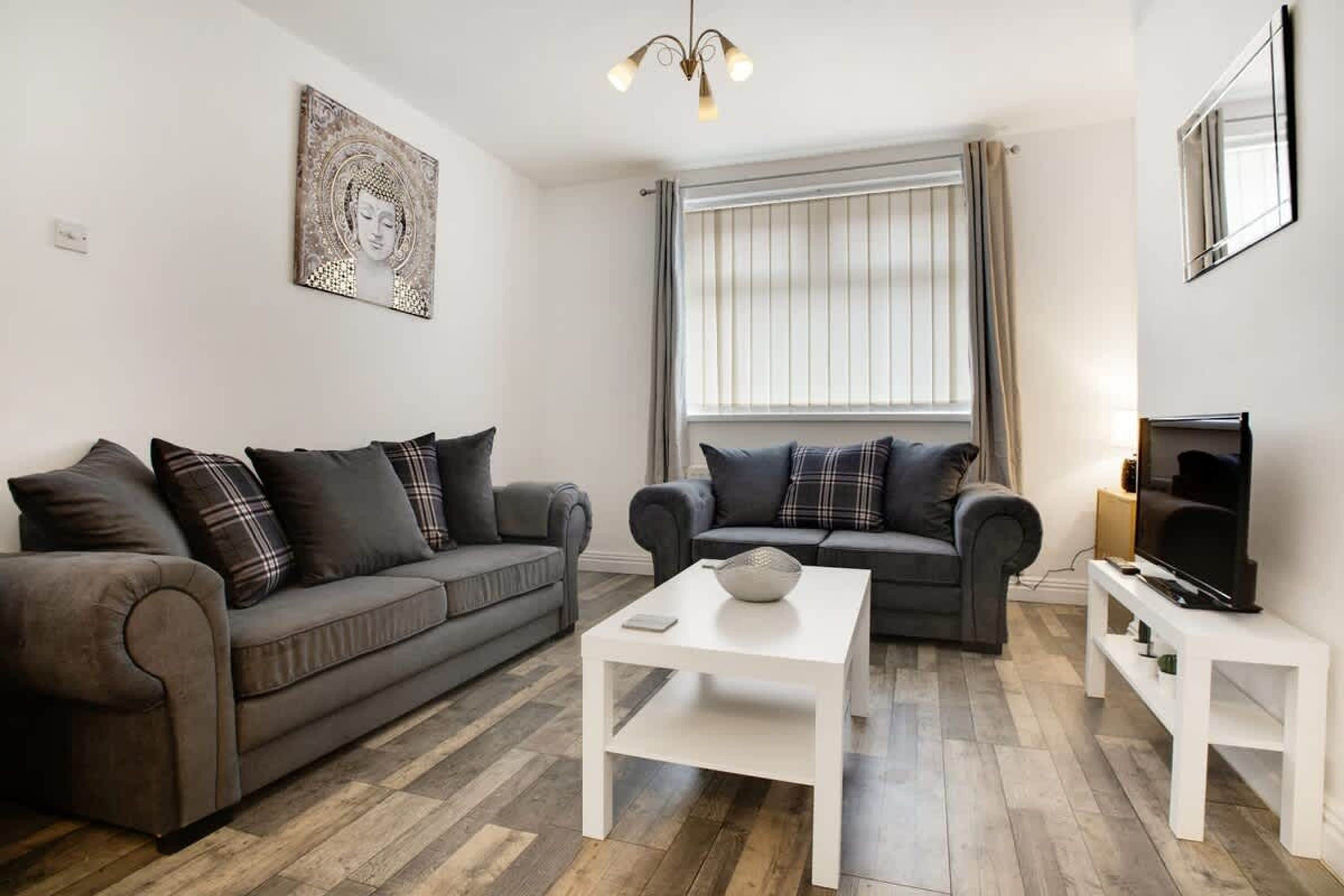 Ein modernes Wohnzimmer mit zwei grauen Sofas, einem weißen Couchtisch und einem Flachbildfernseher auf einem Standfuß.