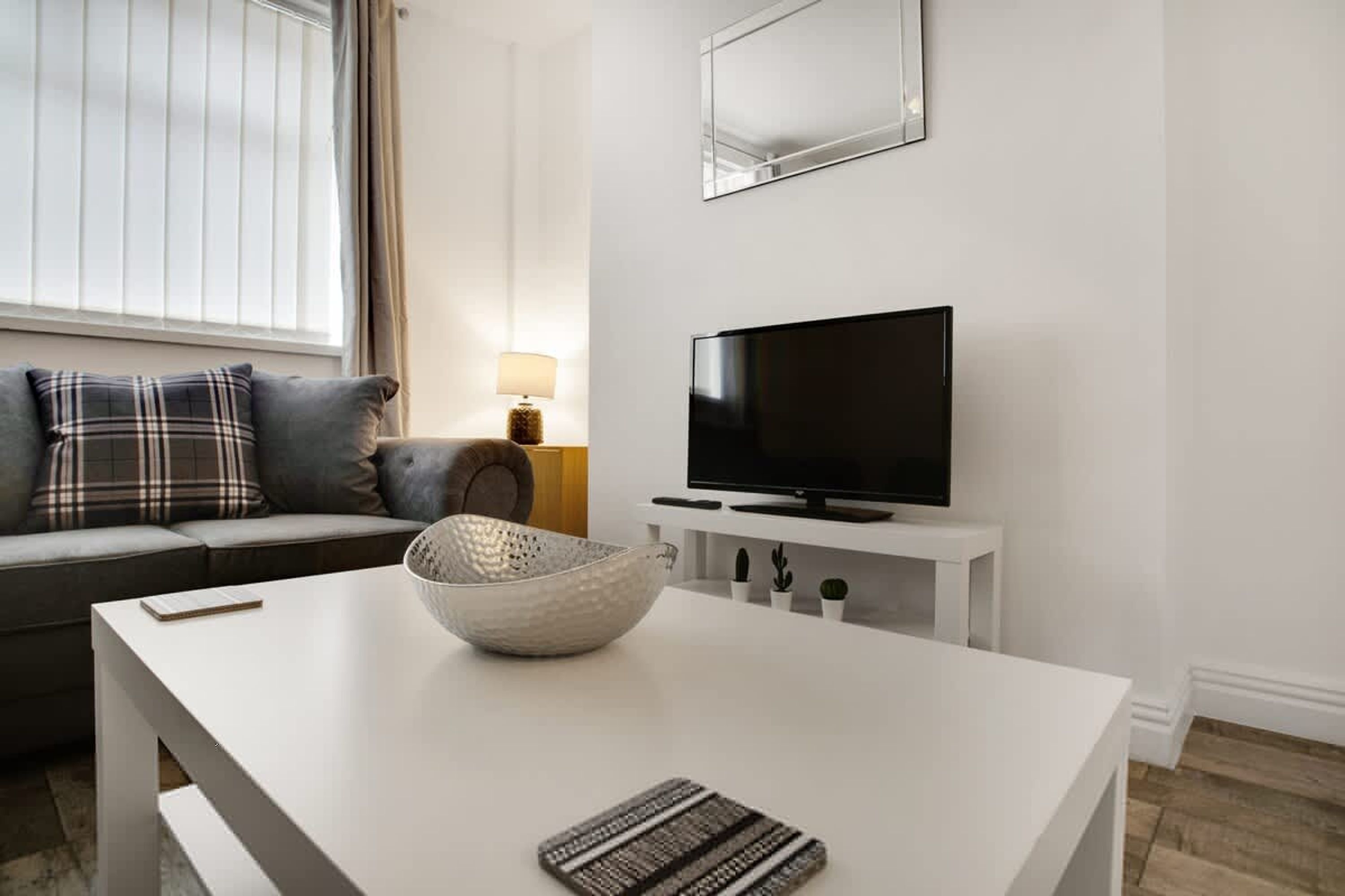A modern living room with a sofa, a flat-screen TV, a white coffee table, and a lamp.