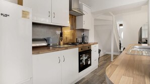 Una cocina moderna con armarios blancos, encimera de madera, horno integrado y campana extractora de acero inoxidable.