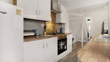 A modern kitchen with white cabinetry, a wooden countertop, a built-in oven, and a stainless steel range hood.