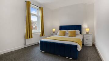 A bedroom with a bed, two bedside tables, a window with curtains, and a radiator.