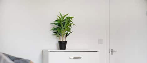 A bedroom with a bed, a bedside table with drawers, a potted plant, and a white wardrobe.