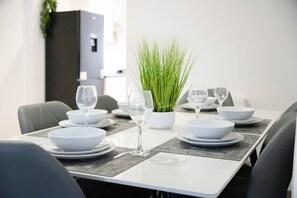 Una mesa de comedor dispuesta con platos, tazones y copas de vino, junto a una planta en maceta.