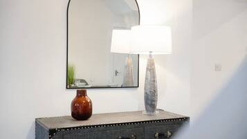 A mirror with a simple black frame, a vase with a white lampshade, and a small, dark-colored cabinet with two drawers.