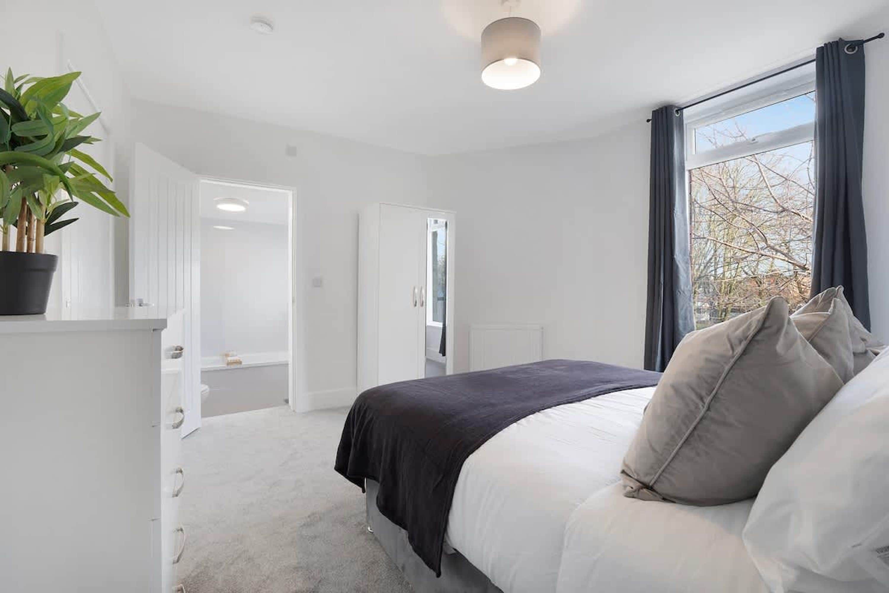 A bedroom with a bed, a potted plant, and a window with curtains.