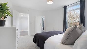A bedroom with a bed, a potted plant, and a window with curtains.