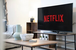 Una sala de estar con un televisor de pantalla plana mostrando el logotipo de Netflix, una mesa de centro con un tazón y un jarrón, un sofá y una mesita auxiliar con una lámpara.