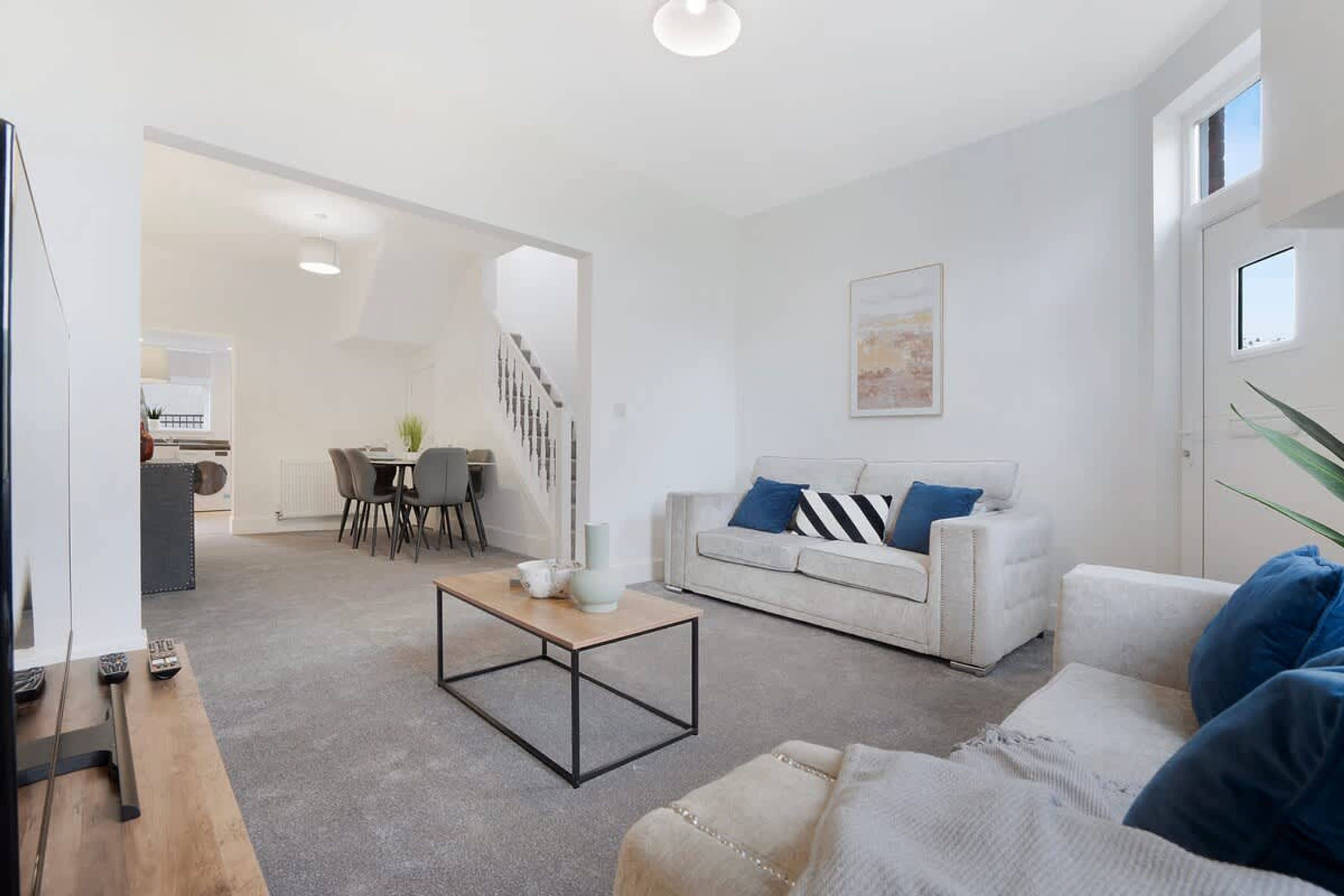 A modern living room with a sofa, coffee table, and a dining area with chairs and a table.