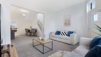 A modern living room with a sofa, coffee table, and a dining area with chairs and a table.