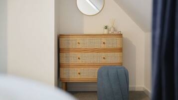 Une pièce avec une commode en bois, un miroir rond et un pouf bleu.