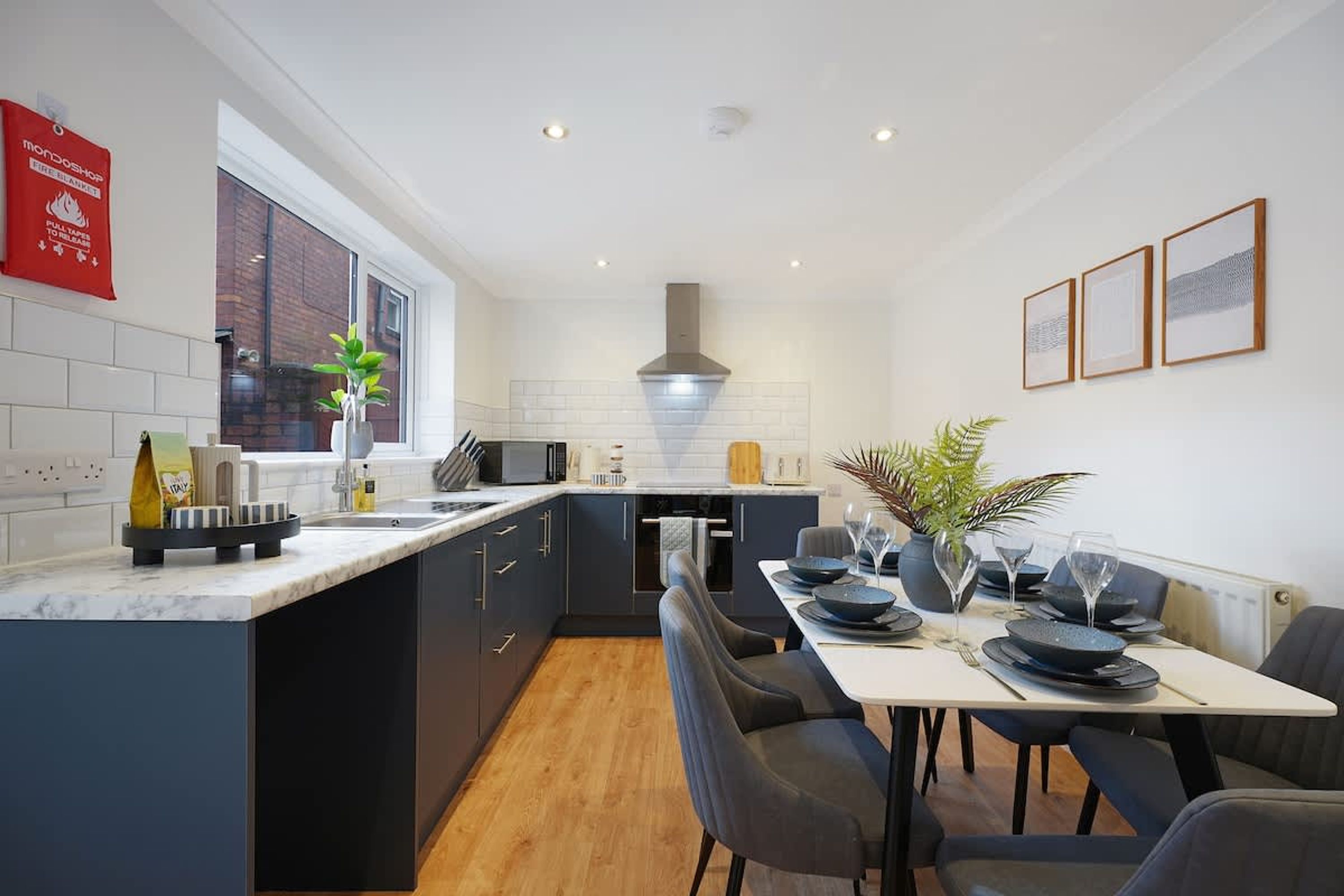 A modern kitchen with a central island, a dining area with a table set for four, and a large window providing natural light.
