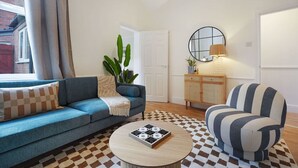 Una sala de estar con un sofá azul, un sillón a rayas, una mesa de centro redonda y un tapete de cuadros.