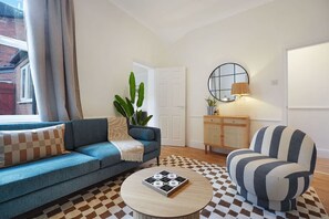 Ein Wohnzimmer mit einem blauen Sofa, einem gestreiften Sessel, einem runden Couchtisch und einem karierten Teppich.