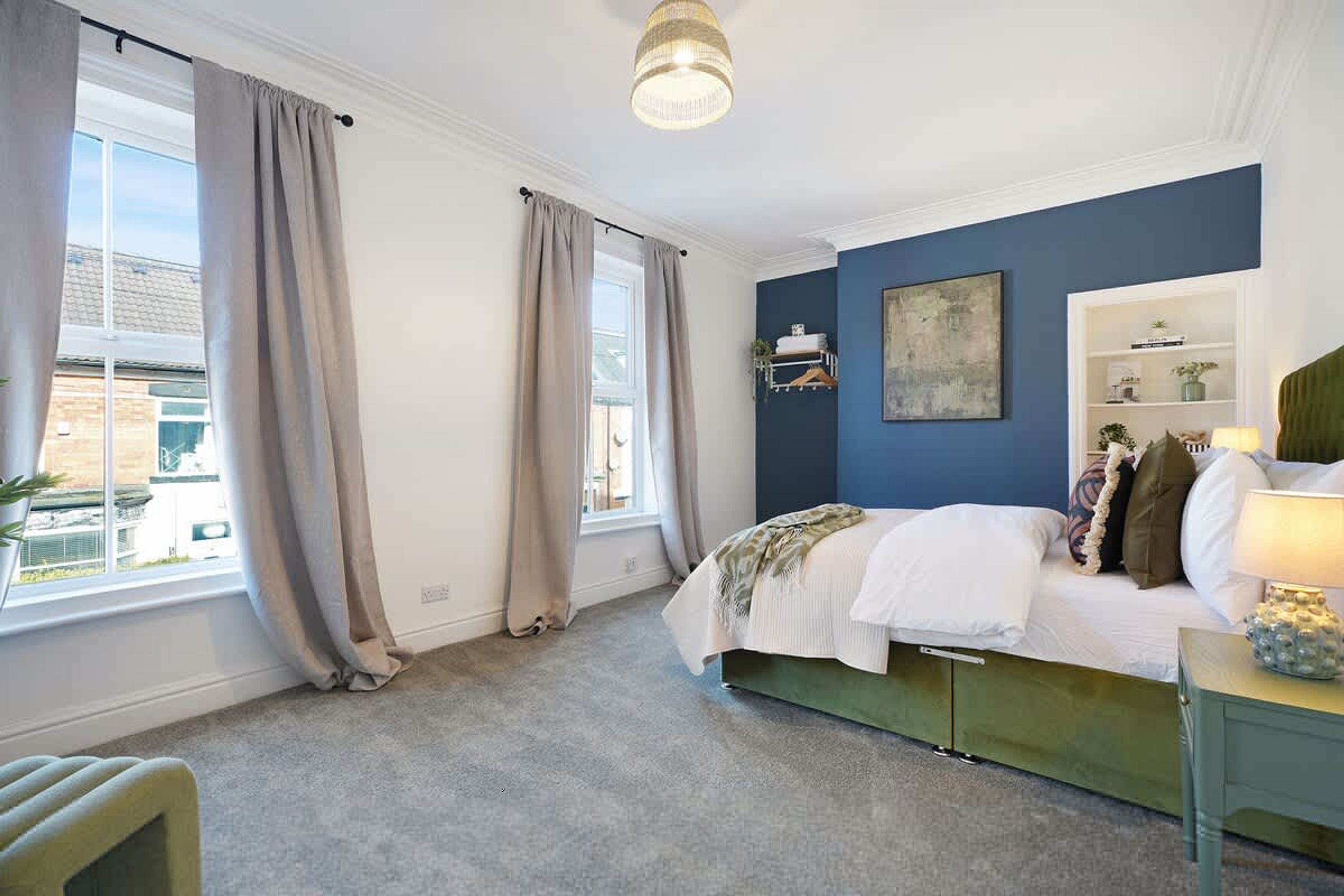 A bedroom with a bed, a bedside table, a lamp, a window with curtains, and a wall with a painting.