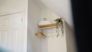 Una puerta blanca, un estante de madera con una planta, y una planta colgante.