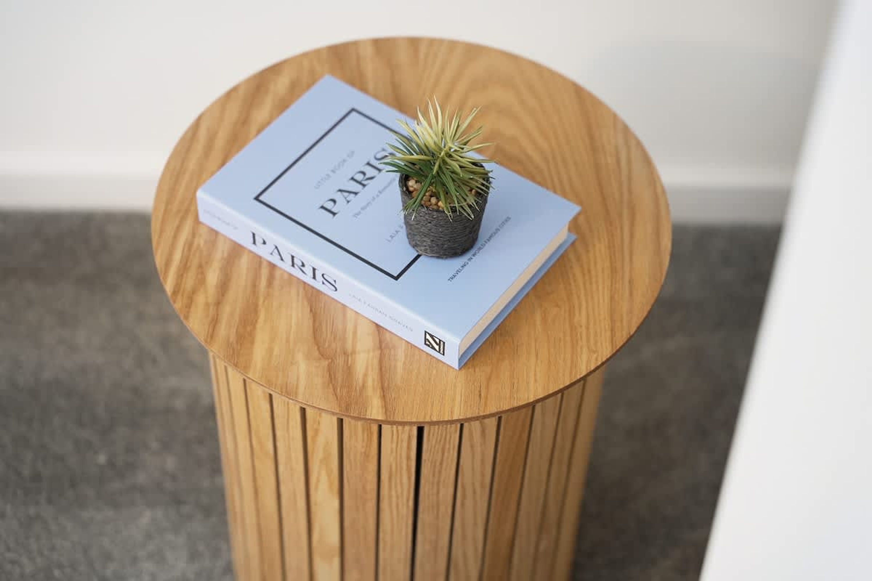 Ein runder Holztisch mit einem Buch mit dem Titel 'PARIS' und einem kleinen Topfpflanzen darauf.