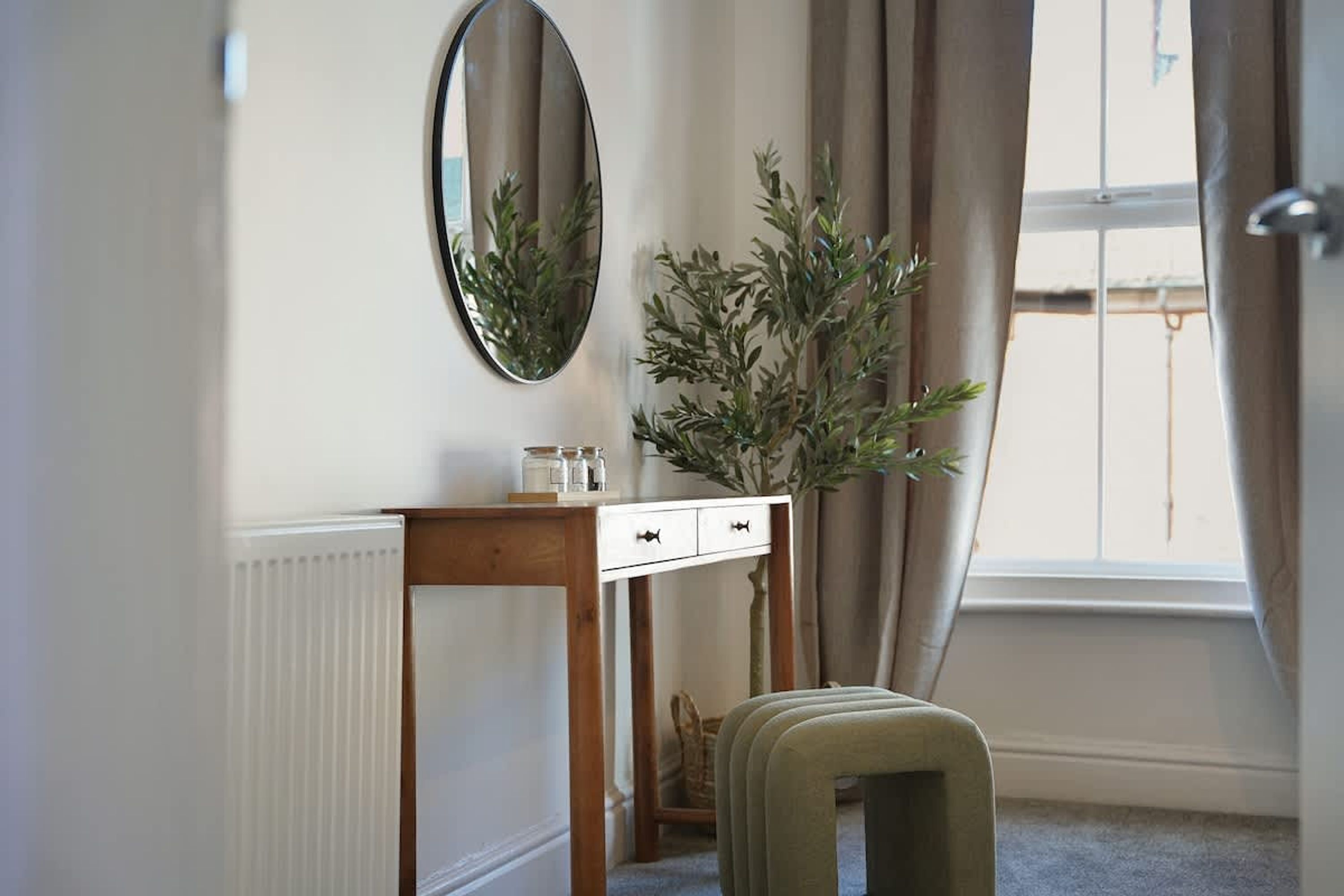 A room with a white dresser, a mirror, a potted plant, and a window with curtains.
