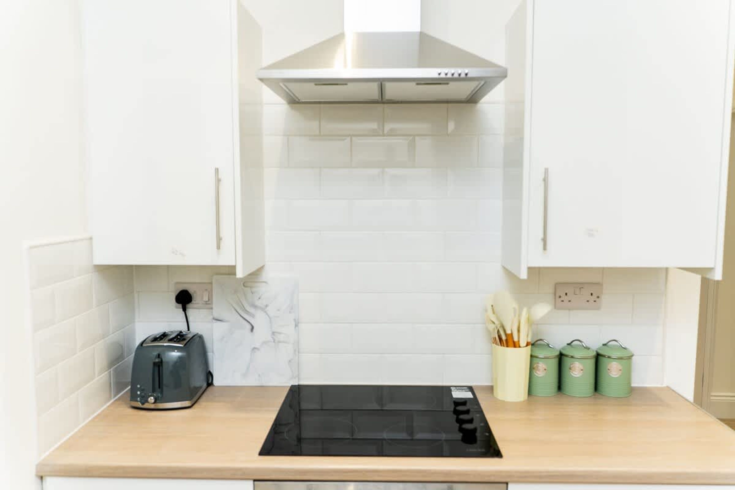 A kitchen with white cabinets, a black induction cooktop, a toaster, and green storage containers.