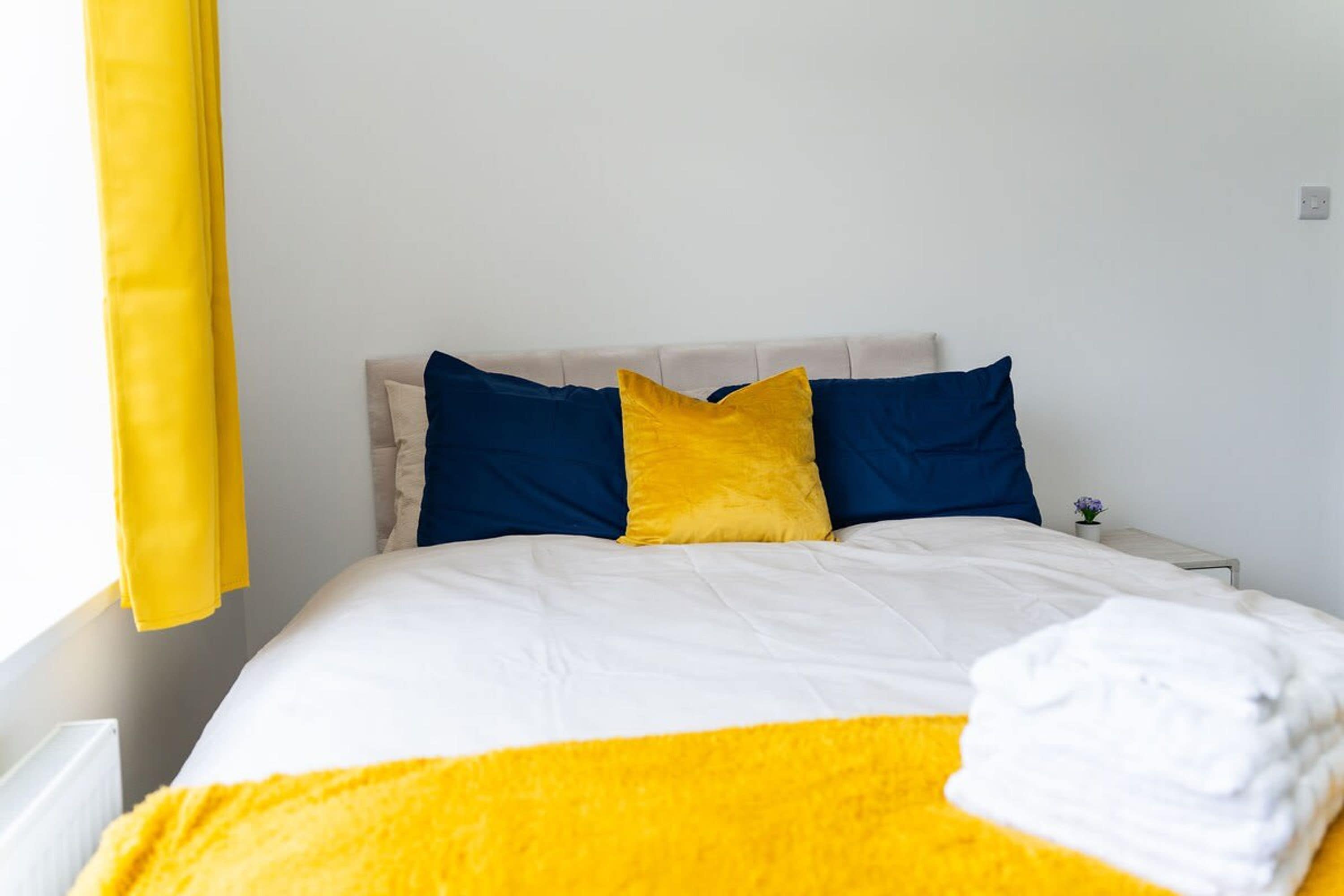 A bed with white and yellow bedding, two blue pillows, and a yellow throw blanket.