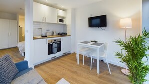 Un espacio habitable compacto con kitchenette, comedor y televisor montado en la pared.