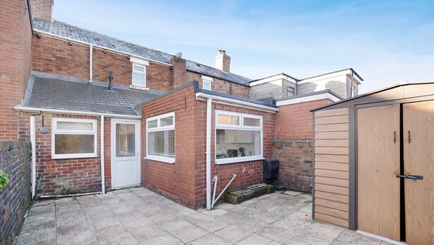 A residential property with a brick exterior, a tiled patio, and a wooden shed. - New 2BR in 53 Rowlington Terrace (Ashington)