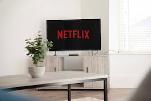 A flat-screen TV with the Netflix logo on a stand in a room with light-colored walls and a window. - New 2BR in 53 Rowlington Terrace (Ashington)