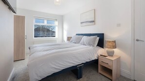 A bedroom with a bed, bedside table, lamp, window, and a door. - New 2BR in 53 Rowlington Terrace (Ashington)