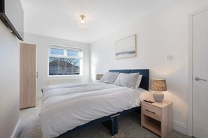 Ein Schlafzimmer mit Bett, Nachttisch, Lampe, Fenster und Tür.