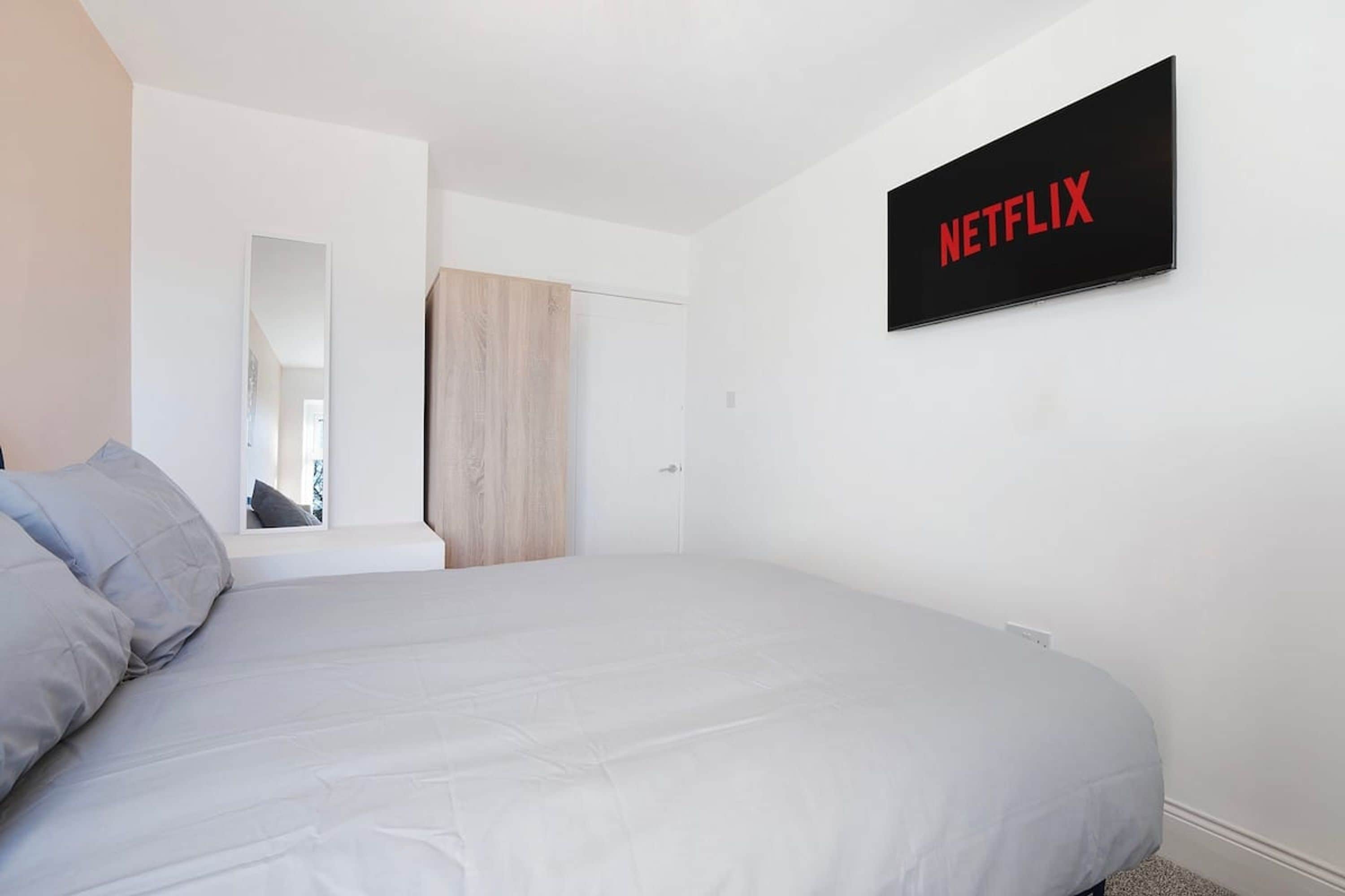 Quarto com cama, sinal de Netflix na parede, porta e espelho.