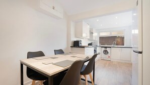 A modern kitchen with a dining area, including a table with chairs, a washing machine, and a refrigerator. - New 2BR in 53 Rowlington Terrace (Ashington)